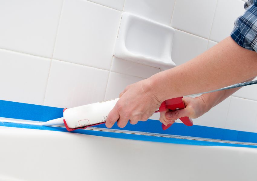 maintenance worker using caulk to fix bathroom grout