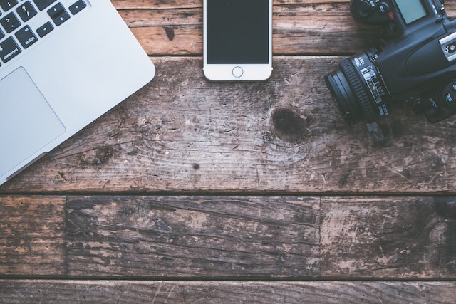 open laptop, cell phone and camera on a wooden desk