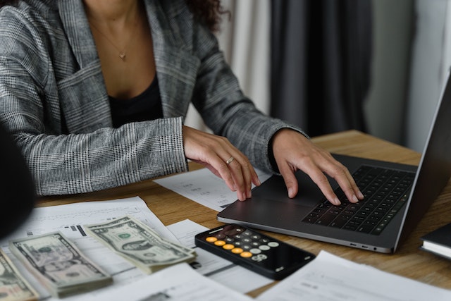 person working on their laptop with a calculator and money next to them
